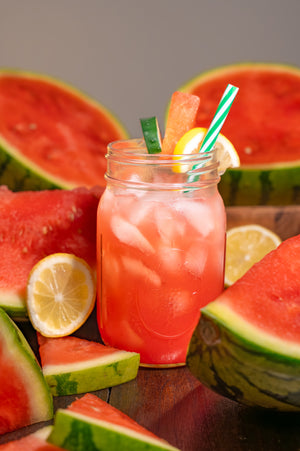 Mason jar filled with watermelon juice surrounded by watermelon slices and lemon wedges on a wooden surface.