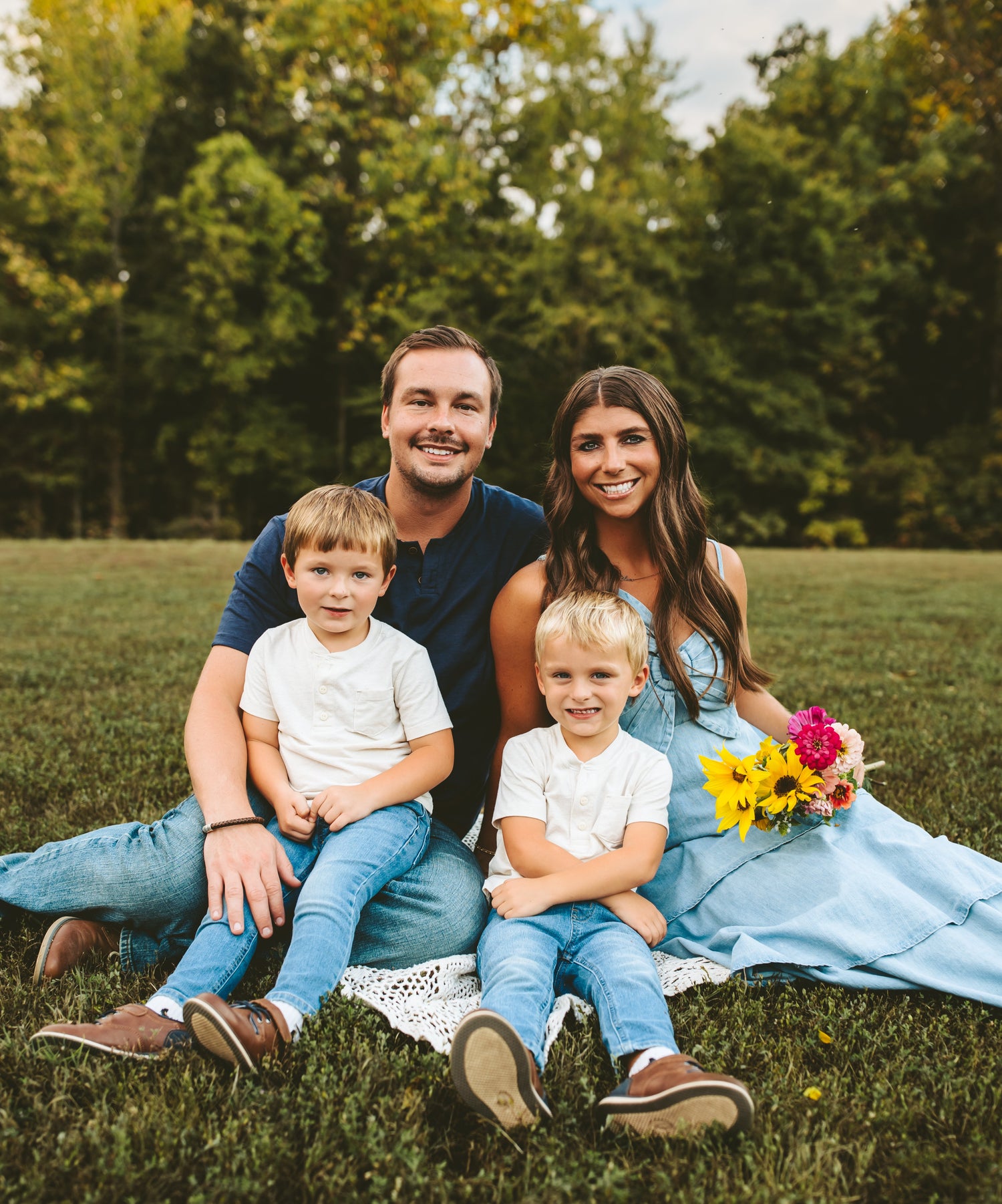 The founder with family sitting on a blanket in a park with trees and grass in the background.